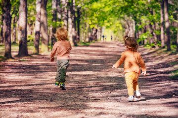 Obraz premium Boy and a girl run on an alley in park view from behind
