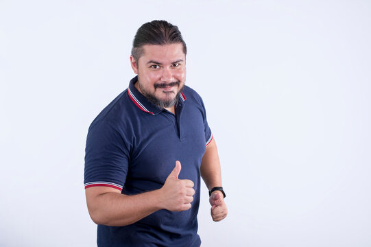 A Confident Man In A Blue Polo Shirt Makes An Assuring Thumbs Up. Mixed Race Man In His 30s. Isolated On A White Background.