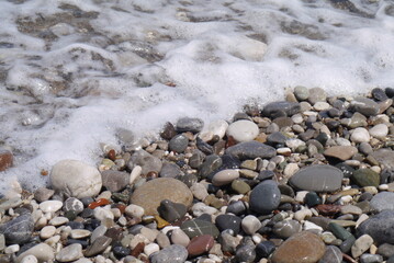 Wet pebbles on the beach with sea foam from the wave