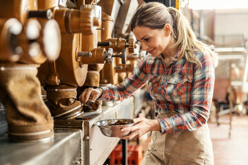 A happy female factory worker measuring ground coffee in facility.