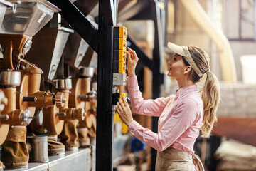 Obraz na płótnie Canvas A female operator starting coffee grinding machine in factory.