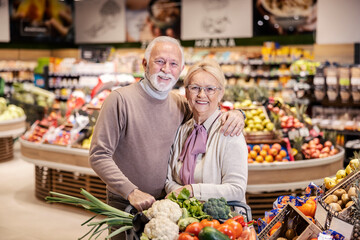 Senior couple hugging and shopping in supermarket while smiling at the camera.