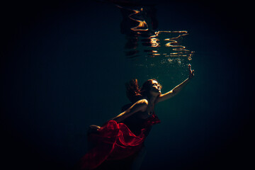 Art work. Underwater shot of a sports girl in lingerie with red material in the pool with beautiful...