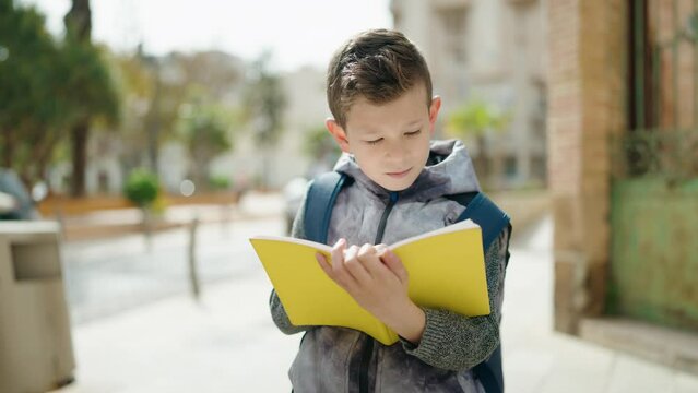 Blond child student reading book standing at street