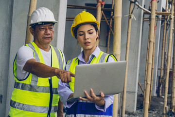 senior male foreman consulting an apprentice engineer with a laptop looking at construction...