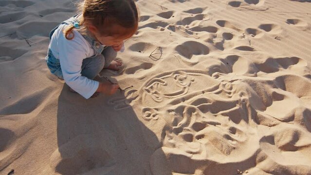 Toddler girls draws pictures on the sand