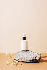 White serum bottle on natural stone with gypsophila flowers on neutral beige background, close up