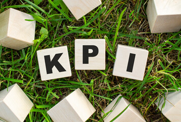 The word KPI is written on wooden cubes. The blocks are located on green grass with sunlight.