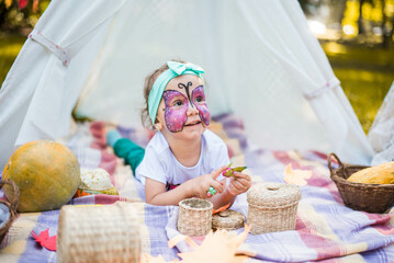 Beautiful girl with a body art face painting butterfly. A rustic autumn still life with pumpkins in basket. Harvest or Thanksgiving. autumn decor, party.