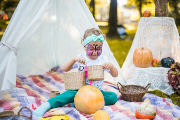 Beautiful girl with a body art face painting butterfly. A rustic autumn still life with pumpkins in basket. Harvest or Thanksgiving. autumn decor, party.
