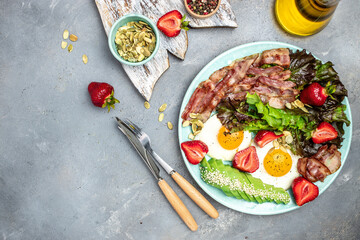 Keto breakfast fried egg, bacon, avocado, strawberries and fresh salad on a light background. banner, menu, recipe place for text, top view