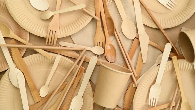 Disposable paper plates, cups and wooden cutlery, top view, rotating

