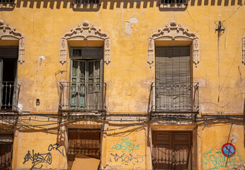 Fototapeta na wymiar Facade of an old building with balconies and windows very deteriorated, with graffiti and cracks on the yellow facade