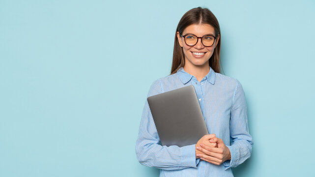 Smart woman in spectacles with gray laptop in hands standing over blue background