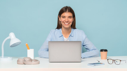 Adorable female online consultant sitting at table with office supplies working on laptop