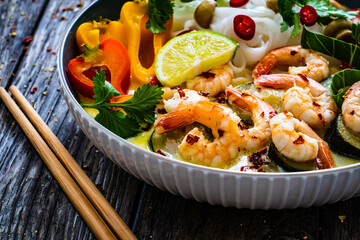 Tom Kha - Thai soup with prawns and rice noodles on wooden table
