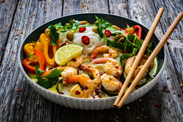 Tom Kha - Thai soup with prawns and rice noodles on wooden table
