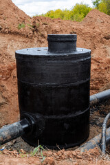A black well stands in the ground, a deep clay pit under the pipeline, a hydropower supply unit of the city, a concrete well, bitumen protective properties against erosion.
