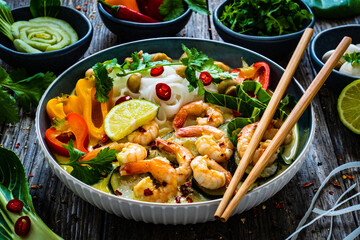 Tom Kha - Thai soup with prawns and rice noodles on wooden table

