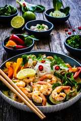 Tom Kha - Thai soup with prawns and rice noodles on wooden table
