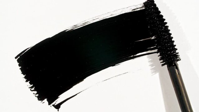 Macro shot and slow motion of a black mascara isolated on white background. Advertising professional cosmetics. Closeup of a mascara wand on white background. High quality 4k footage