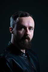 dramatic portrait of bearded millennial guy in leather jacket on dark background