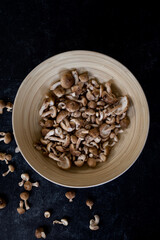 Top view of mixture of wild shiitake mushrooms in bamboo bowl on dark black background.