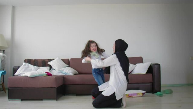 A Muslim mother in a hijab and her daughter are dancing in the room. The little girl put on red high heels. Muslim family
