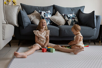 Little caucasian girl 7 years old and her baby sister 1 year old. Toddler kid playing with sibling...