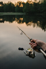 Fishing day. Fishing for pike, and perch from a lake, river or pond. Background wild nature. Fisherman with rod, spinning reel catches fish from a pier or boat. Article about concept of rural getaway.