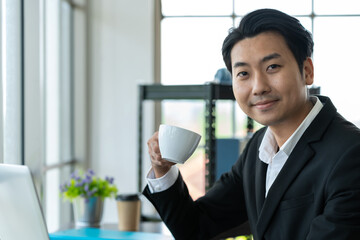 Smile Asian business man drinking coffee and working with laptop computer at the workspace office.