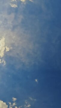 Looking up at a beautiful Summer sky with thick, heavy clouds moving vertically. Backdrop of a perfect blue sky.