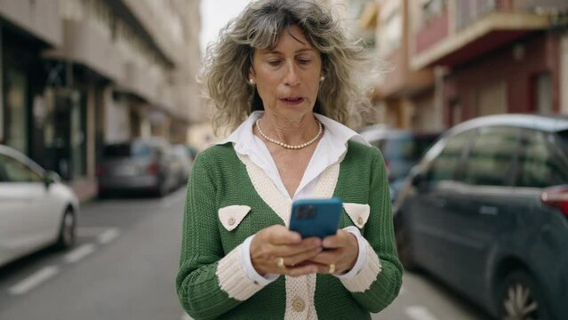 Middle age woman smiling confident using smartphone at street