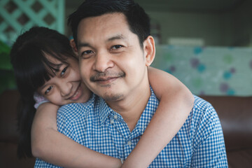 Fototapeta premium Father and daughter are hugging with love, looking at camera and smiling while sitting on sofa at home.Concept of Father's day