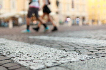 Stone pavement in perspective. Old street paved with stone blocks with white lines. Shallow depth of field. Vintage grunge texture. City ​​and people on background.