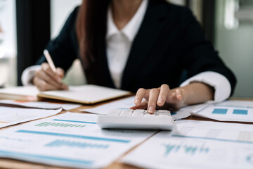 Close up of businessman or accountant hand holding pen working on calculator and laptop computer to calculate business data during make note at notepad, accountancy document at office
