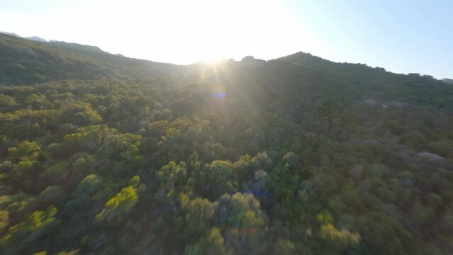 FPV video, view from above, aerial view from an FPV drone flying at high speed over some mountains and green hills illuminated during a beautiful sunset. Sardinia, Italy.