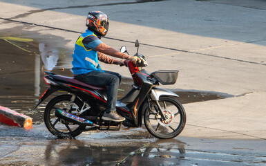 The mototaxi driver in a blue vest ride on the wet street