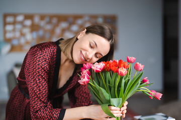 Beautiful woman arranging flowers presented by her husbant at home, happy and joyful