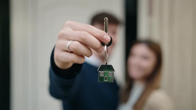 Young couple standing together holding key of new home at street