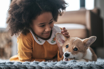 A curly-haired girl in orange dress playing with a puppy
