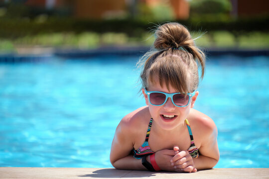 Portrait of happy child girl relaxing on swimming pool side on sunny summer day during tropical holidays