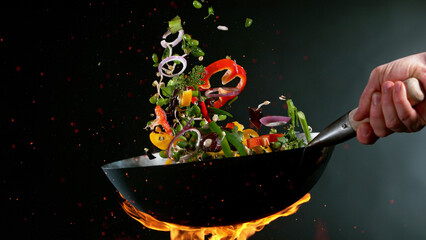 Closeup of chef throwing vegetable mix from wok pan in fire. - obrazy, fototapety, plakaty