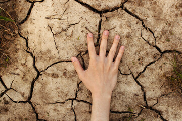 Cracked dry ground and young man hand. Photo was taken 25 May 2022 year, MSK time in Russia.