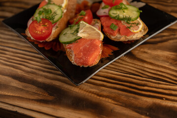 Sandwiches with red fish and vegetables lie on the plates. Dark wood background.