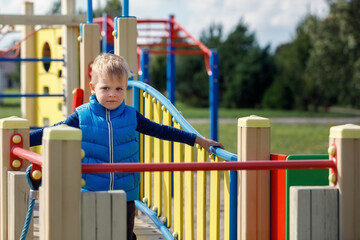 A cute, blond child walks in the modern colorful outdoor playground. The happy boy spends his free...