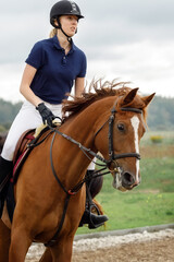 A young girl with a helmet rides a horse in a riding competition. Portrait up close at high riding speed and horse motion