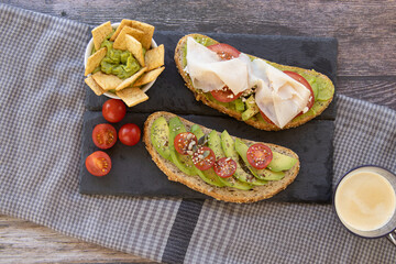 Sliced and diced avocado toast with a guacamole spread, tomato, cherry tomatoes, turkey breast, pico, slate stone plate, with a cloth on the table.
