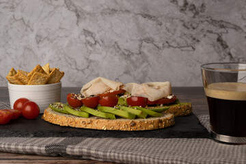 Sliced and diced avocado toast with a guacamole spread, tomato, coffee, cherry tomatoes, turkey breast, pico, slate stone plate, with a cloth on the table.