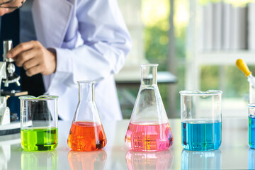 Chemistry laboratory glassware with colour liquids with Research scientists looking into microscopes